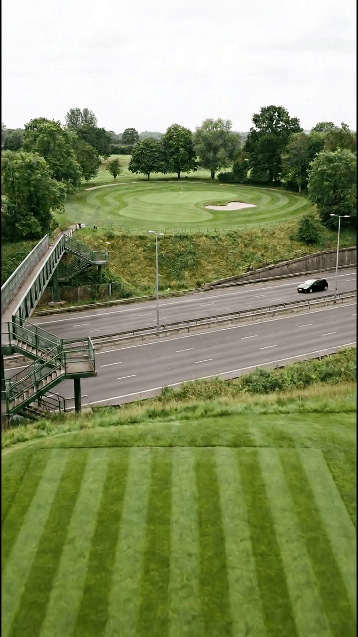 A par 3 played from a striped tee on high ground straight across a six lane German autobahn running through a cutting, to a green with a single bunker on the ground opposite, a green steel footbridge crossing the road on the left
